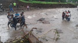 Sekelompok anak muda mengevakuasi motor melewati Kali Magerepu akibat jembatan darurat di lokasi itu hanyut terbawa banjir bandang, Selasa (29/1)
