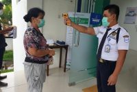 Petugas keamanan pada Kantoe BPJS Kesehatan Maumere sedang mengukur suhu tubuh salah satu peserta JKN-KIS
