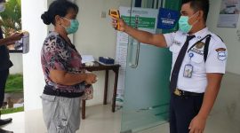 Petugas keamanan pada Kantoe BPJS Kesehatan Maumere sedang mengukur suhu tubuh salah satu peserta JKN-KIS
