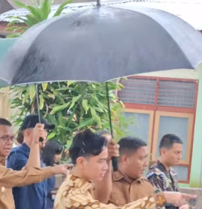 Bupati Sikka Juventus Prima Yoris Kago memayungi Wapres Gibran Rakabuming Raka saaat hujan deras di SMAS Bhaktyarsa, Selasa (6/5)