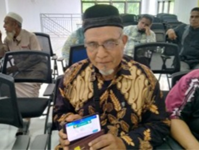 Aruji Umar, peserta JKN yang kini menjadi calon jemaah haji, memperlihatkan Kartu Indonesia Sehat